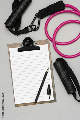 Expanders for fitness and elastic bands for sports, as well as an open notebook with a pen for drawing up a training schedule on a gray background. The concept of drawing up a sports training plan