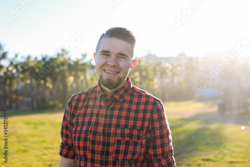 Handsome young smiling man standing on the grass at park. Summer in the city concept.