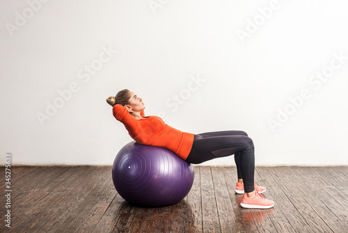 Slim sporty young woman in tight sportswear lying on big fitness rubber ball, stretching and exercising abdomen muscles in gym home. Health care, sports activity and workouts. indoor studio shot photo