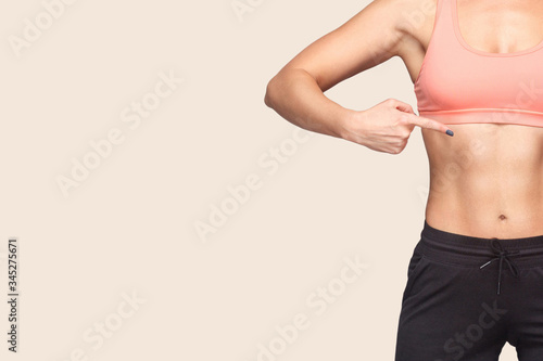 Closeup of fit woman wearing sports tight top and pants pointing herself, showing slim athletic body with trained abdominal muscles, copy space for advertising workouts in gym, weight loss. Healthcare photo