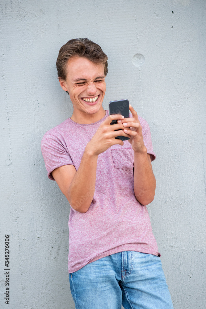 Fototapeta premium smiling young man leaning against wall looking at cellphone