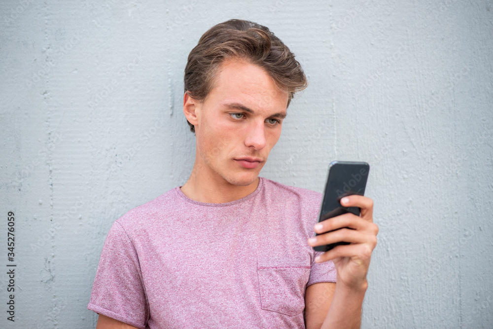 Close up serious young man leaning against wall looking at cellphone Close up serious young man leaning against wall looking at cellphone