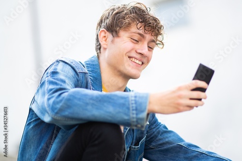 Close up smiling young man sitting outside looking at mobile phone