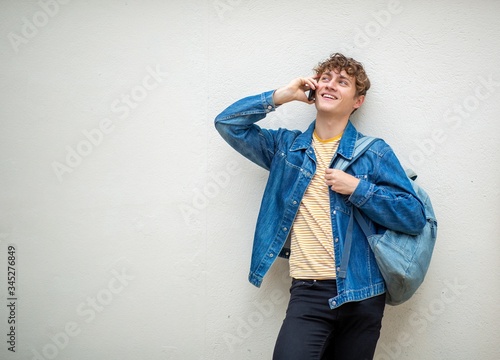 happy guy with bag talking with mobile phone by wall