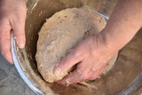 Close up of a baker kneading bread dough in a metal bowl. 
Handmade bread dough in a stainless steel bowl.
