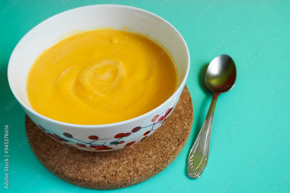 yellow soup - mashed pumpkin, potatoes, carrots, onions and cream in a white plate on a light blue background with a metal spoon on a brown stand . For lunch and dinner . Food for children yellow soup - mashed pumpkin, potatoes, carrots, onions and cream in a white plate on a light blue background with a metal spoon on a brown stand . For lunch and dinner . Food for children