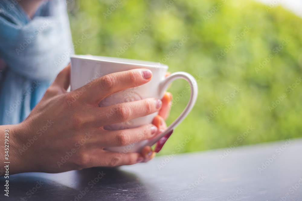 Enjoying a cup of tea: Young girl is sitting on the veranda, holding a mug in her hand Enjoying a cup of tea: Young girl is sitting on the veranda, holding a mug in her hand
