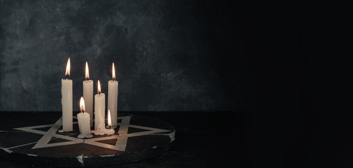 Six burning candles and the Star of David against on a dark gray background wall.