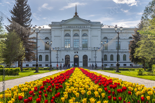 White building of Tomsk State University with tulip flowers in backlight and sunbeams with blue sky