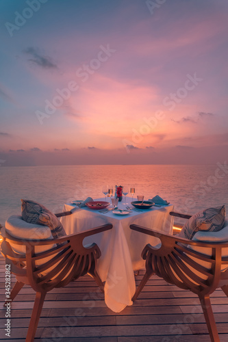 Romantic dinner on the beach with sunset, candles with palm leaves and sunset sky and sea. Amazing view, honeymoon or anniversary dinner landscape. Exotic island evening horizon, romance for a couple 