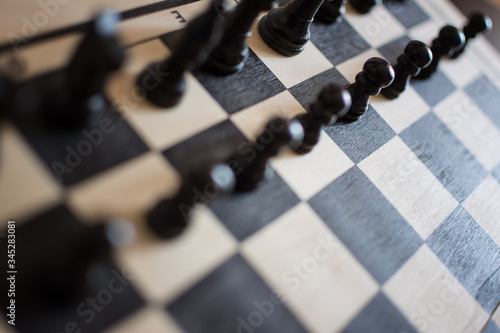 Cropped view of chess board with black chess pieces on rustic wooden surface