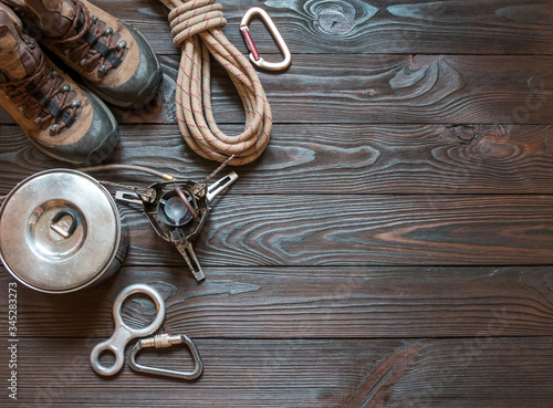 climbing equipment: rope, trekking shoes, carabiners, burner, saucepan and other set on dark wooden background, top view.