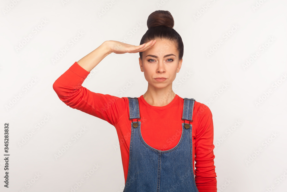 Yes sir! Portrait of strict responsible girl with hair bun in denim overalls giving salute listening to order with serious attentive expression, following discipline. indoor studio shot, isolated Yes sir! Portrait of strict responsible girl with hair bun in denim overalls giving salute listening to order with serious attentive expression, following discipline. indoor studio shot, isolated