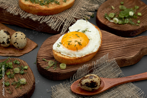 Breakfast eggs on bun, quail eggs, greens on a wooden plate.