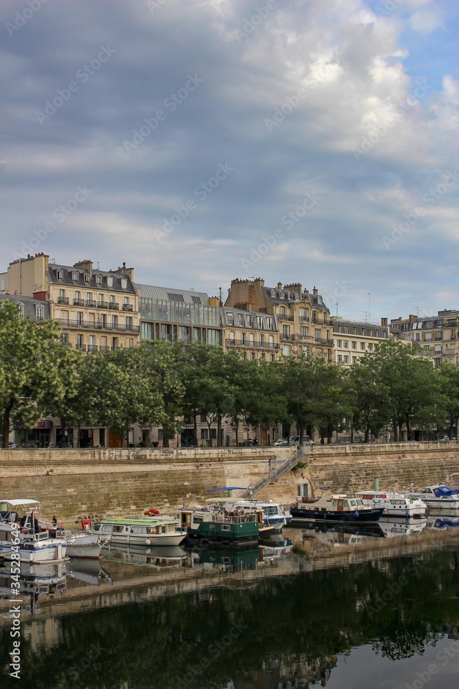 Beautiful, dramatic, darkened photo of the Seine embankment (La Seine) with trees, boats and historic houses in Paris, France