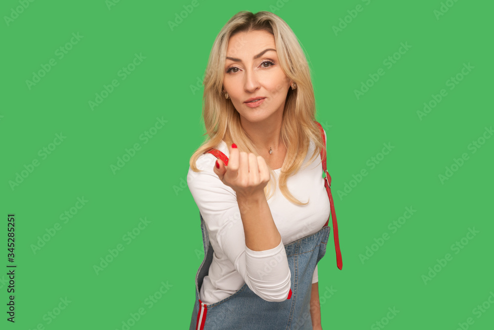 Come here! Portrait of sexy attractive adult woman in stylish denim overalls inviting with beckoning finger gesture and seductive enticing look. indoor studio shot isolated on green background Come here! Portrait of sexy attractive adult woman in stylish denim overalls inviting with beckoning finger gesture and seductive enticing look. indoor studio shot isolated on green background
