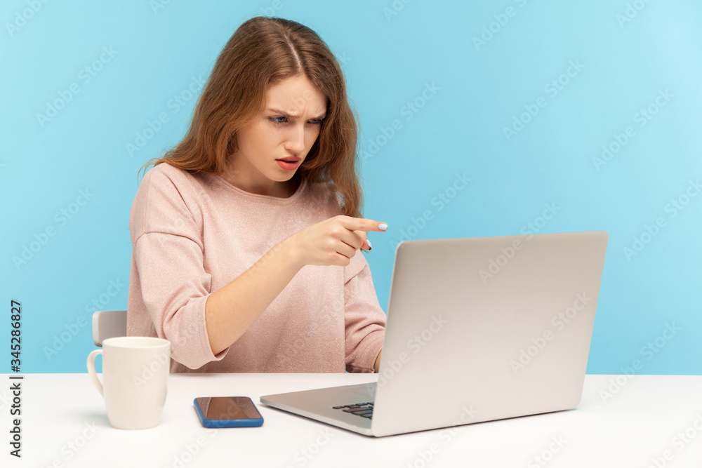 Hey you! Angry businesswoman pointing to laptop screen, scolding and accusing while talking on video call, irritated boss having online conference. indoor studio shot isolated on blue background Hey you! Angry businesswoman pointing to laptop screen, scolding and accusing while talking on video call, irritated boss having online conference. indoor studio shot isolated on blue background