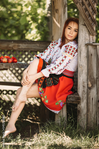 Fotografía Young  redhead moldavian girl dressed in traditional costume resting in a wooden