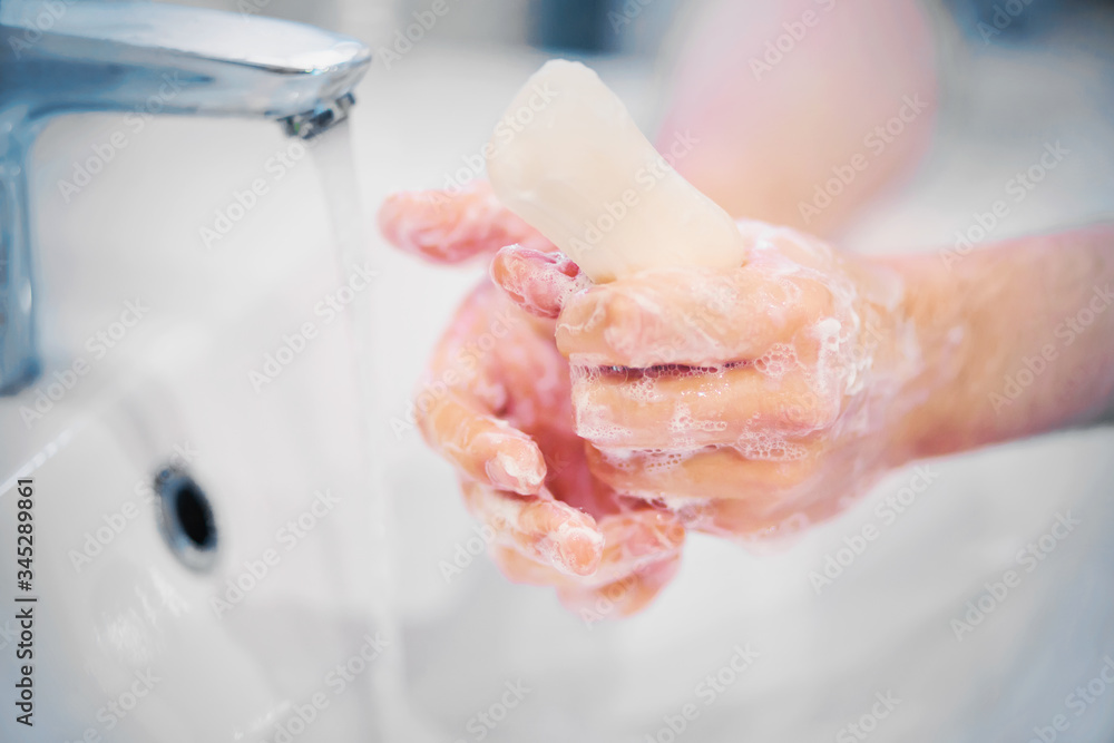 Fototapeta premium A person washes their hands with white gentle soap that foams well, and the tap water flows into the sink. Tenderness and hygiene.