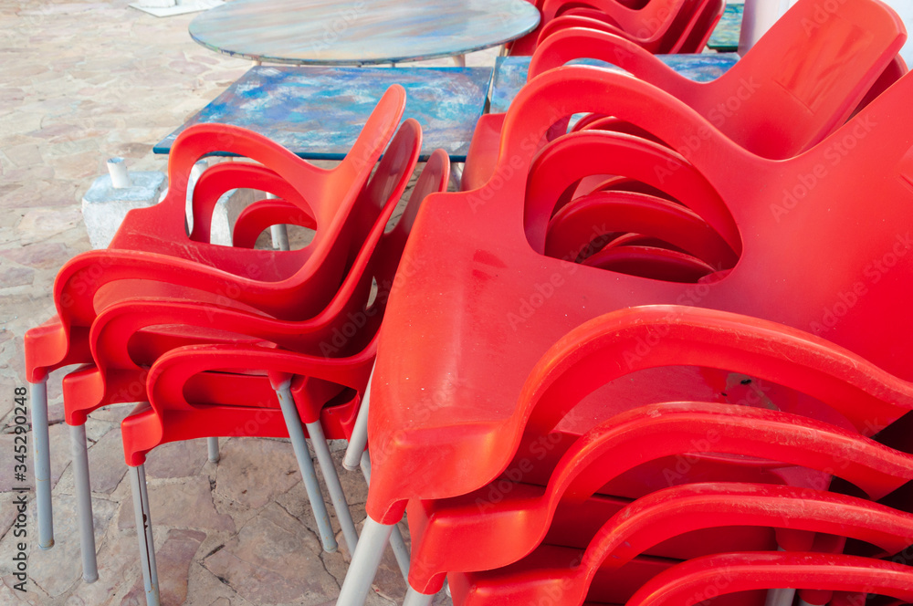 Red plastic chairs stacked next to outdoor tables