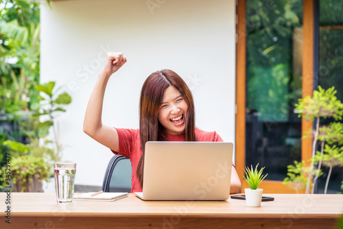 Asian business woman using technology laptop and celebrating when job success form working from home in outdoor home and garden, startups and business owner, social distancing and self responsibility