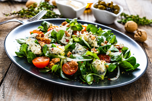 Fresh salad - blue cheese, cherry tomatoes, vegetables and walnuts on wooden background
