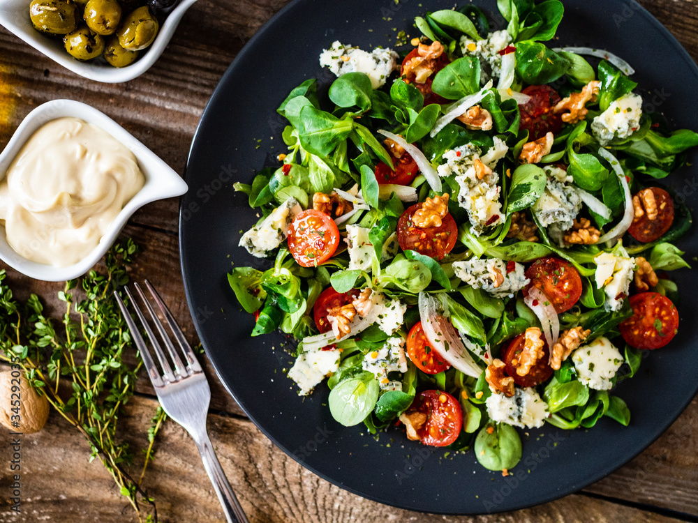 Fresh salad - blue cheese, cherry tomatoes, vegetables and walnuts on wooden background
