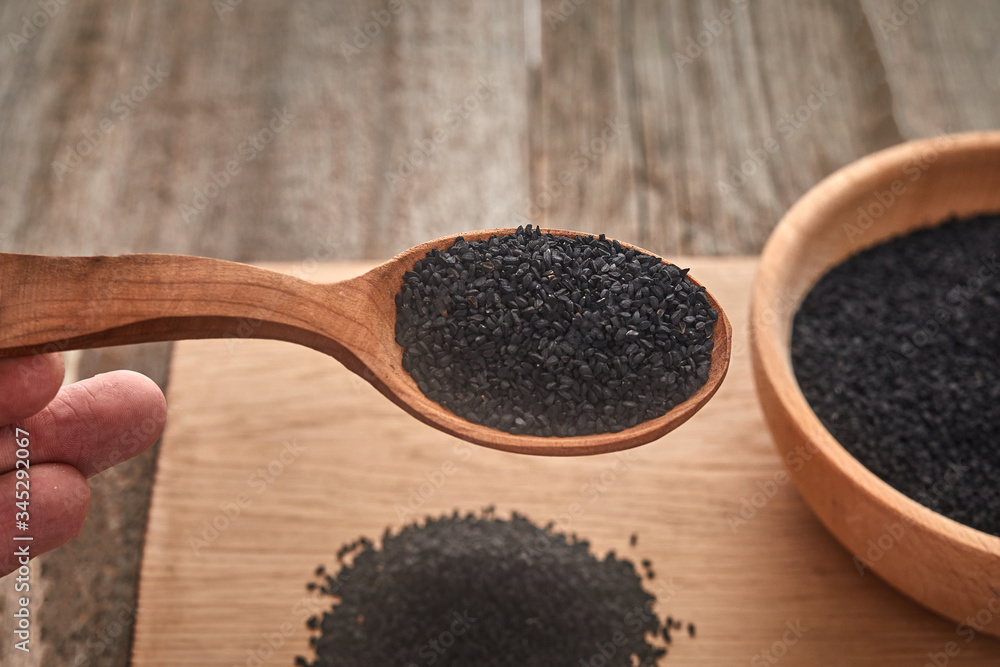 Black cumin seeds and a wooden spoon on a wooden table. Healthy, vegetarian, organic food concept. Black cumin seeds and a wooden spoon on a wooden table. Healthy, vegetarian, organic food concept.