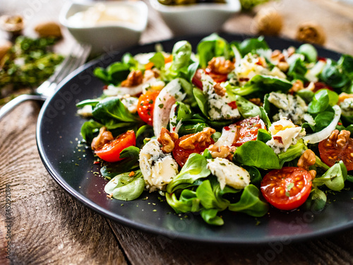Fresh salad - blue cheese, cherry tomatoes, vegetables and walnuts on wooden background 
