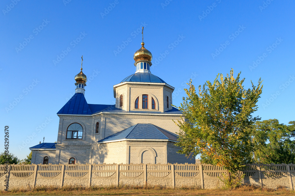 Orthodox church in the village, rural summer landscape. In the evening, before sunset. The concept of religious architecture, Easter, other holidays and various religious denominations in Ukraine.