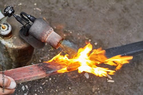 A man is burning the board using the old rusty blowtorch. Handmaking manufacturing process of burnt board
