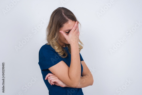 Indoor portrait of beautiful woman with stylish haircut, wearing casual clothes, making facepalm gesture while smiling, standing over gray background amazed with stupid situation.