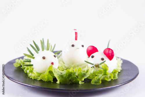 Eggs shaped like animals (with elements made of rosemary, radish, chive) on a plate, on a white background