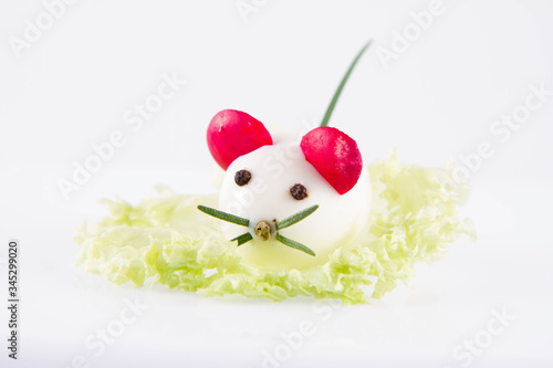 Egg shaped like an animal (with elements made of rosemary, radish, chive) on a lettuce leaf on a white background