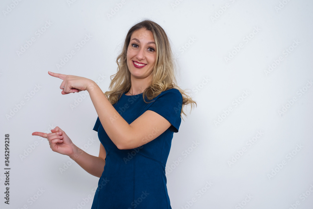 Positive attractive young female, points aside with cheerful and surprised expression with mouth opened, shows something amazing standing indoors. Advertisement concept. Positive attractive young female, points aside with cheerful and surprised expression with mouth opened, shows something amazing standing indoors. Advertisement concept.