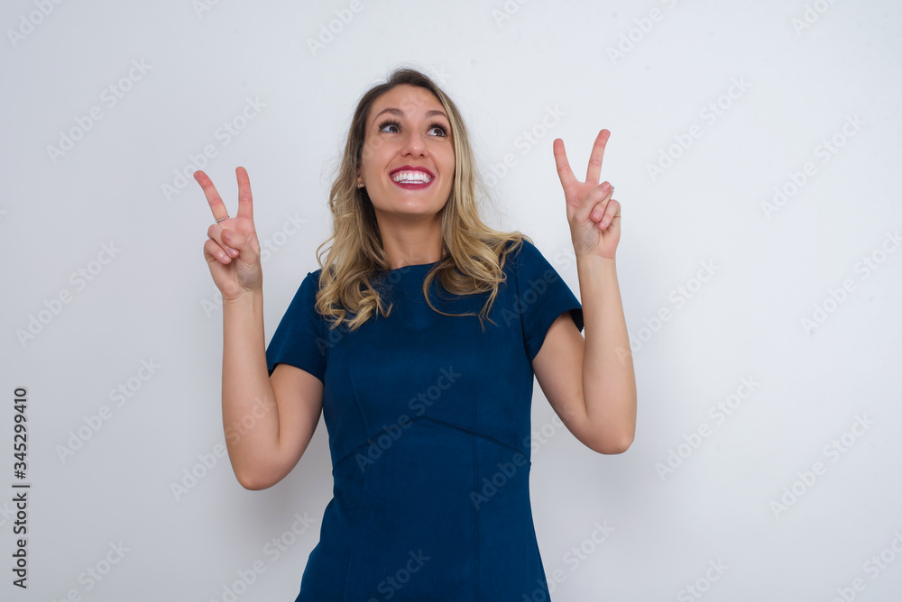 Isolated shot of cheerful woman makes peace or victory sign with both hands, dressed in casual clothes, feels cool has toothy smile, isolated over gray background. People and body language. Isolated shot of cheerful woman makes peace or victory sign with both hands, dressed in casual clothes, feels cool has toothy smile, isolated over gray background. People and body language.