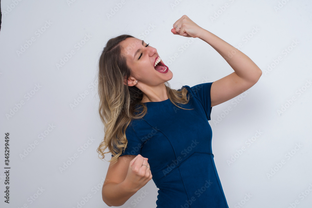 Attractive young caucasian woman celebrating a victory punching the air with her fists and a beaming toothy smile over a white studio background with copy space. Attractive young caucasian woman celebrating a victory punching the air with her fists and a beaming toothy smile over a white studio background with copy space.