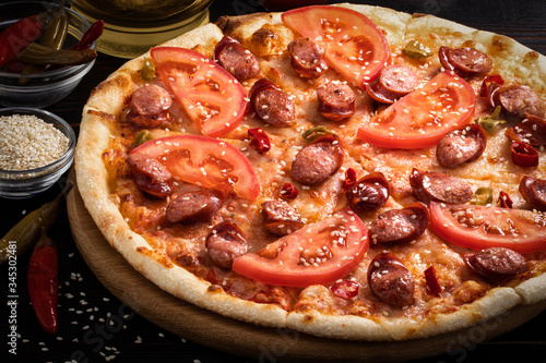 pizza with bavarian sausages, tomato and chili pepper on dark background