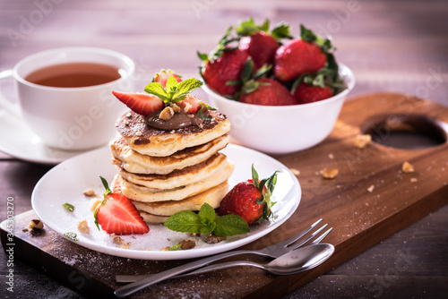 Pancakes with chocolate sauce and fresh strawberries on brawn wooden background. Delicious sweet dessert.
