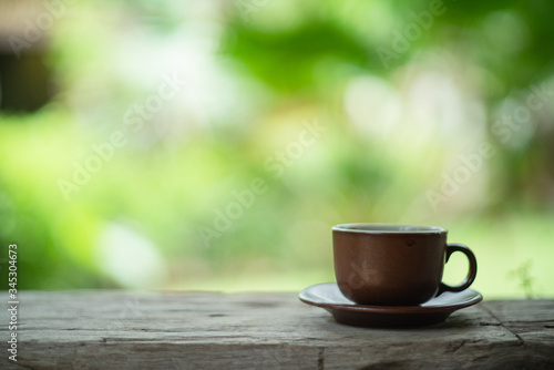 Brown cup of coffee on old wooden floor and green background on sun set