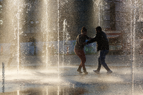  Man and woman dancing in the fountain of the park, back light