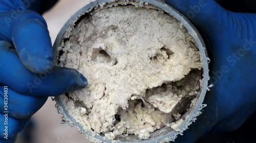 Plumber man in rubber gloves, shows a sewer pipe in section. Fat deposits in the tube. Clogging. Close-up.