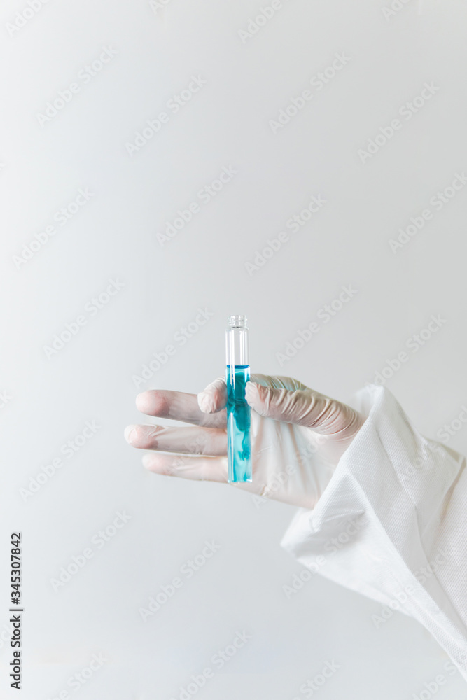 Hand of a nurse doctor or scientist wearing a protective suit and white gloves holding a test tube with blue liquid against white backgeound. Vaccine 
 antidote coronavirus covid-19 pandemic outbreak