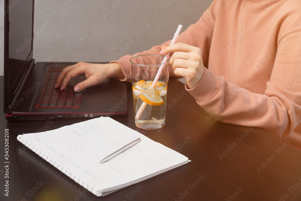 side view girl working on laptop, sitting at a dark table. hand holds a straw for juice. manager work concept side view girl working on laptop, sitting at a dark table. hand holds a straw for juice. manager work concept