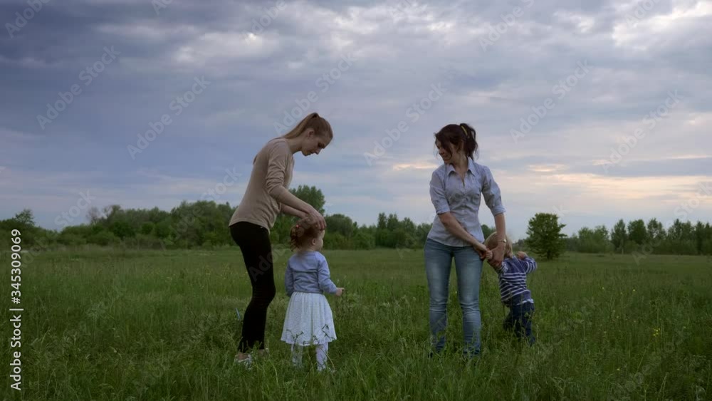 Mothers play with Children on Nature in the Grass Field. Evening Cloudy Sunset Sky Mothers play with Children on Nature in the Grass Field. Evening Cloudy Sunset Sky