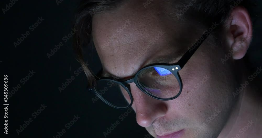 Handsome male with glasses working on a laptop late at night Handsome male with glasses working on a laptop late at night