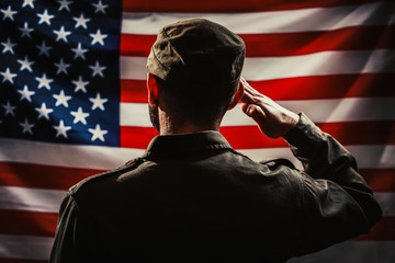 Memorial day. A uniformed soldier salutes against the background of the American flag. Rear view. Dark colors. The concept of the American national holidays and patriotism