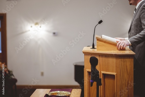 Fotografia Male in a grey suit preaching words of the Holy Bible at the altar of a church