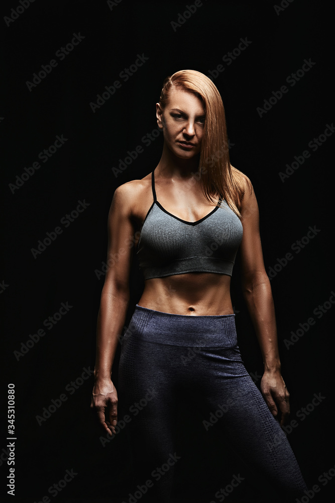 Sporty woman portrait in dark sportswear on a dark background. Beautiful body, sport banner, low key, copy space. Sporty woman portrait in dark sportswear on a dark background. Beautiful body, sport banner, low key, copy space.