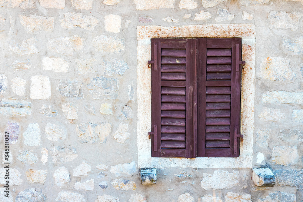 Authentic house with a stone wall, with beautiful old open windows and with green shutters, and with vases on the window.